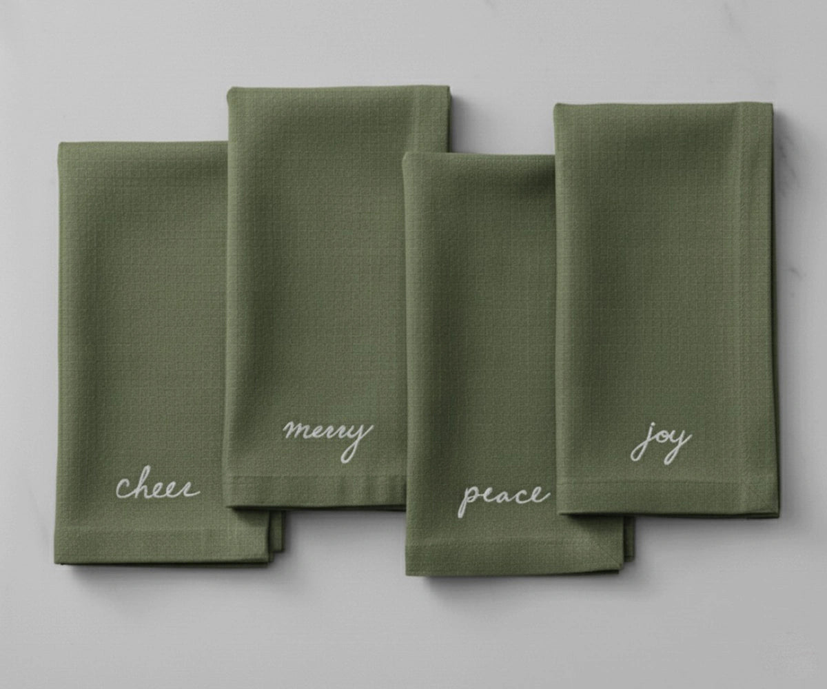 Soft light green festive napkin with crisp white embroidered holiday wording for a cheerful table setting.