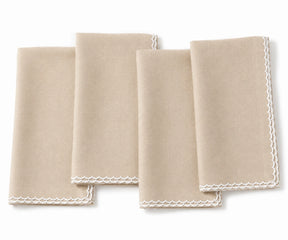 Four folded beige cloth napkins with white scalloped edges, arranged overlapping on a white background.