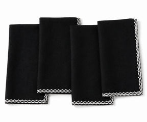 Four black square cloth napkins with white scalloped edges, arranged overlapping on a plain white background.