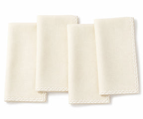 Four ivory colored cotton napkins with delicate embroidered borders, arranged overlapping on a white background.