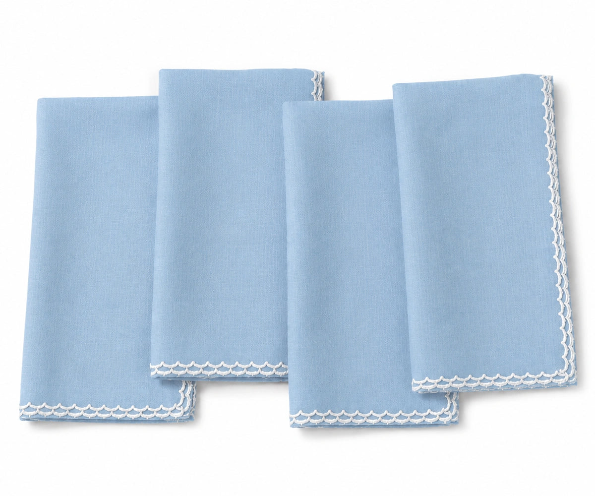 Four light blue cloth napkins with white scalloped edges, arranged overlapping on a white background.