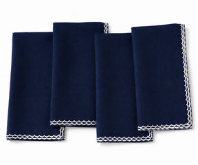 Four navy blue napkins with white embroidered borders, arranged in an overlapping fan layout on a white background.
