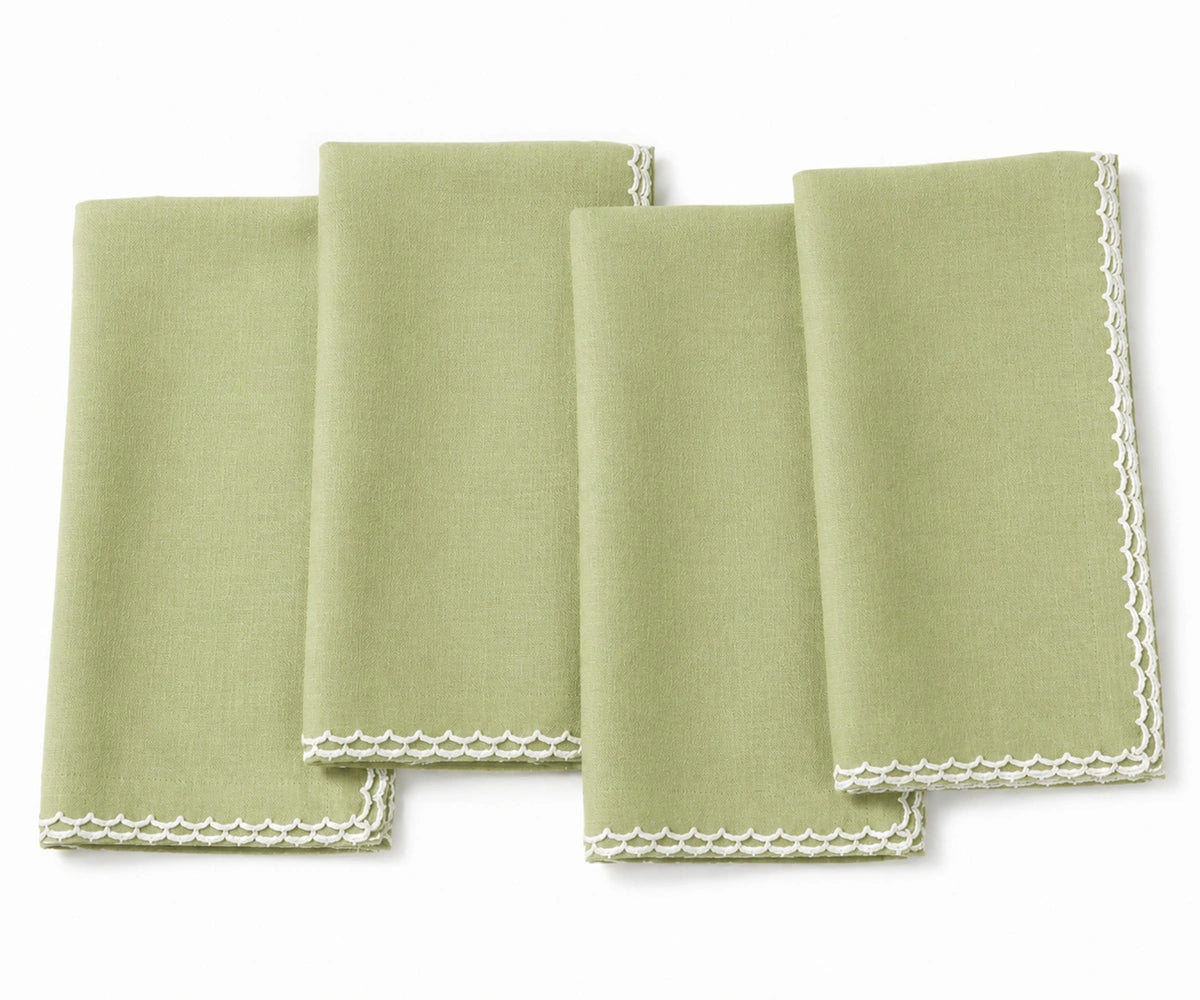 Four folded pista green cloth napkins with white scalloped lace edges, arranged on a white background.