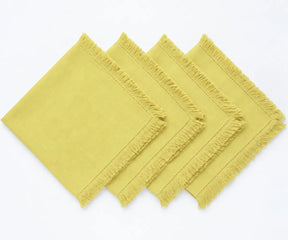 Butter yellow cotton napkins with decorative fringe trim styled beside white dinnerware and floral accents for a spring dining table.