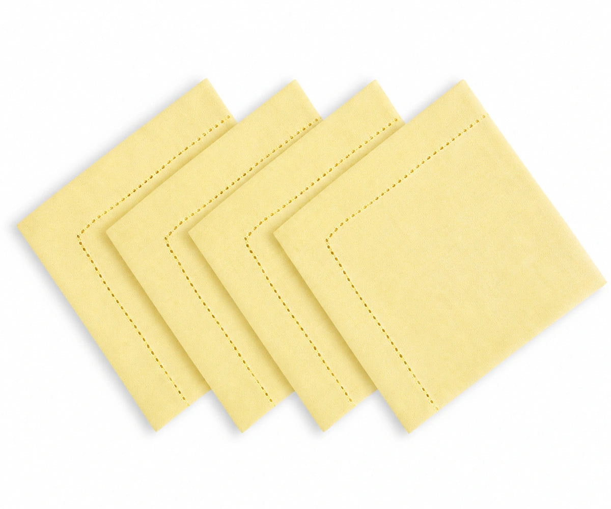 Four butter yellow square napkins with decorative border stitching, arranged in a staggered fan layout on a white background.