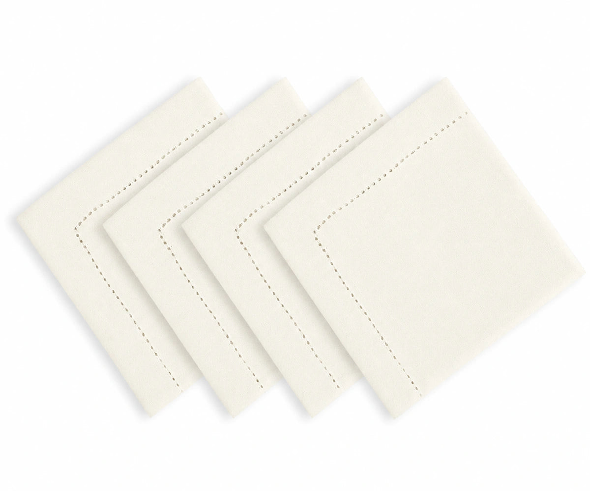 Four ivory-colored square napkins with delicate dashed border stitching, arranged in a staggered fan pattern on a solid white background.