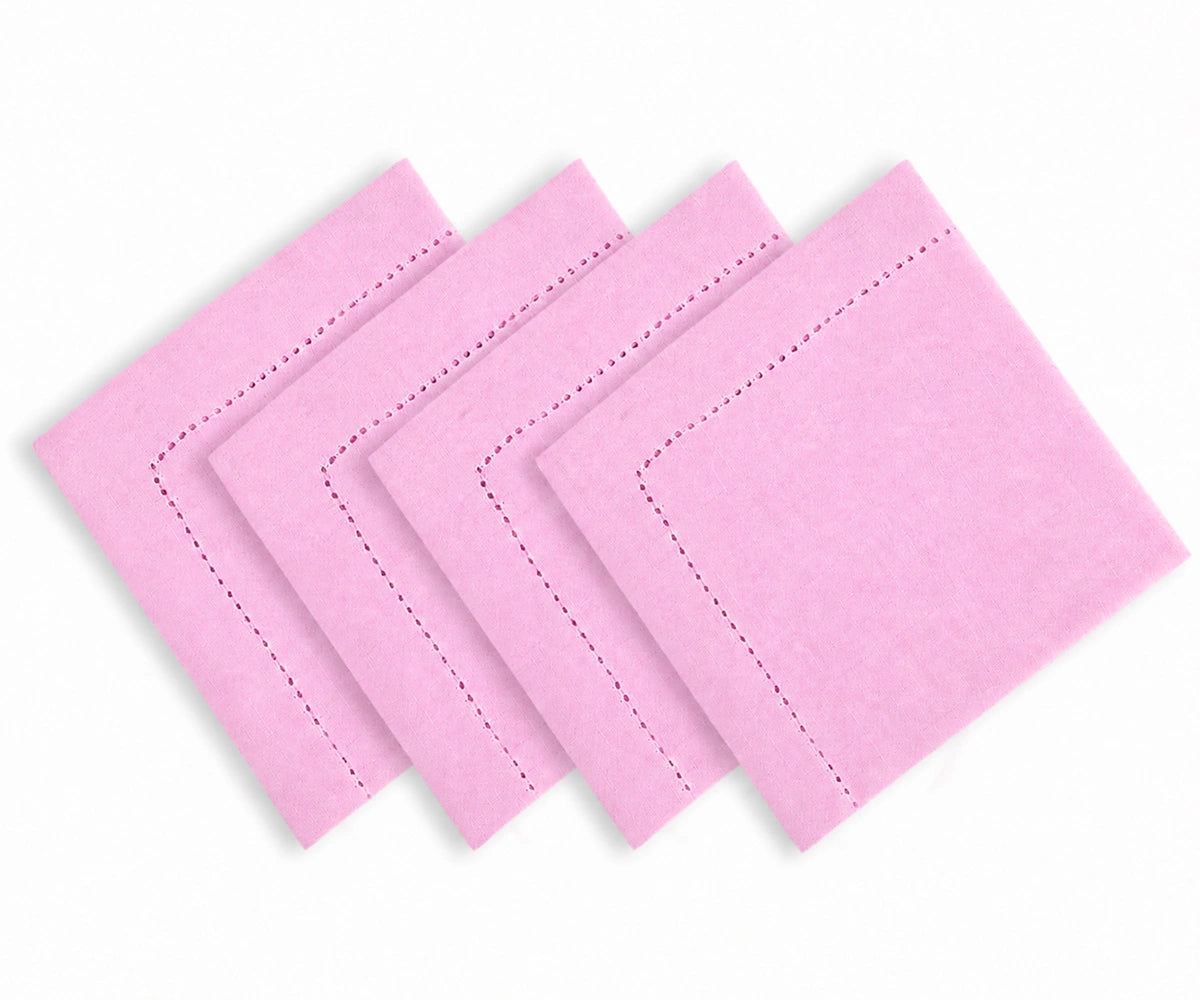 Four light pink square napkins with decorative dashed border stitching, arranged in a staggered stack on a white background.