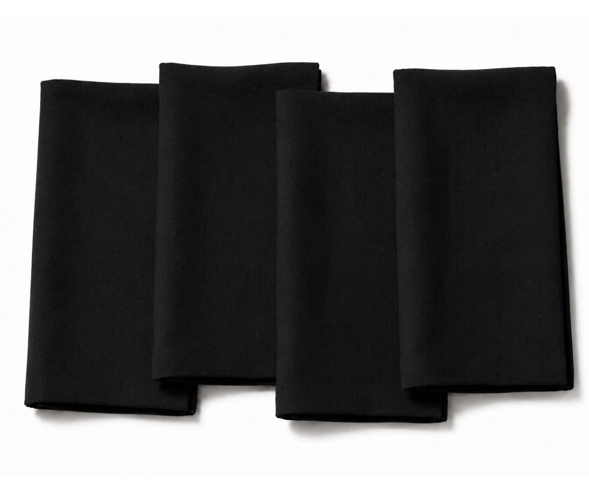 Set of four folded black cotton dinner napkins arranged on a white background.