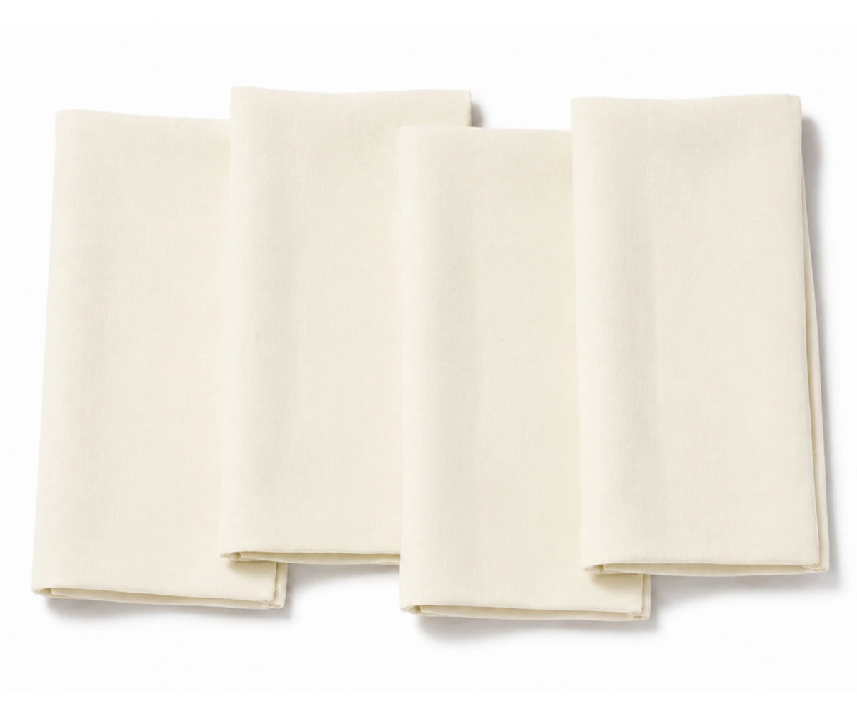 Set of four folded ivory cotton dinner napkins arranged on a white background.