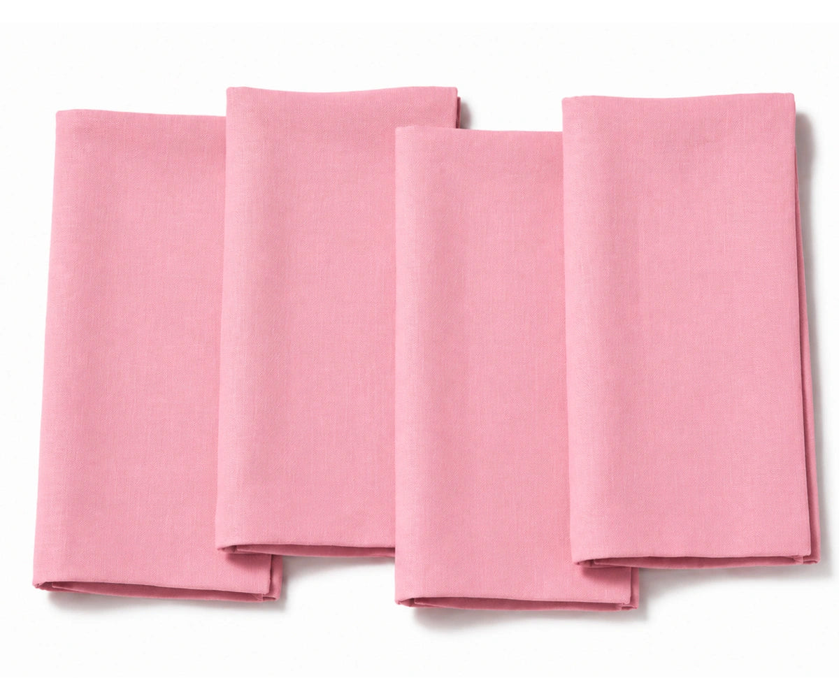Set of four folded light pink cotton dinner napkins arranged on a white background.