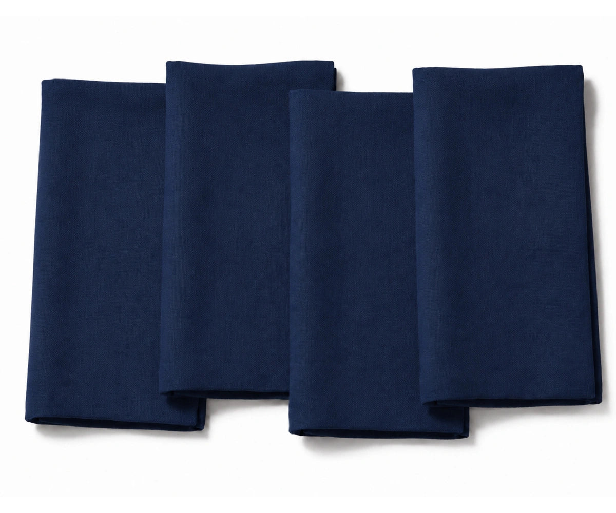 Set of four folded navy blue cotton dinner napkins arranged on a white background.