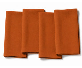 Set of four folded rust cotton dinner napkins arranged on a white background.