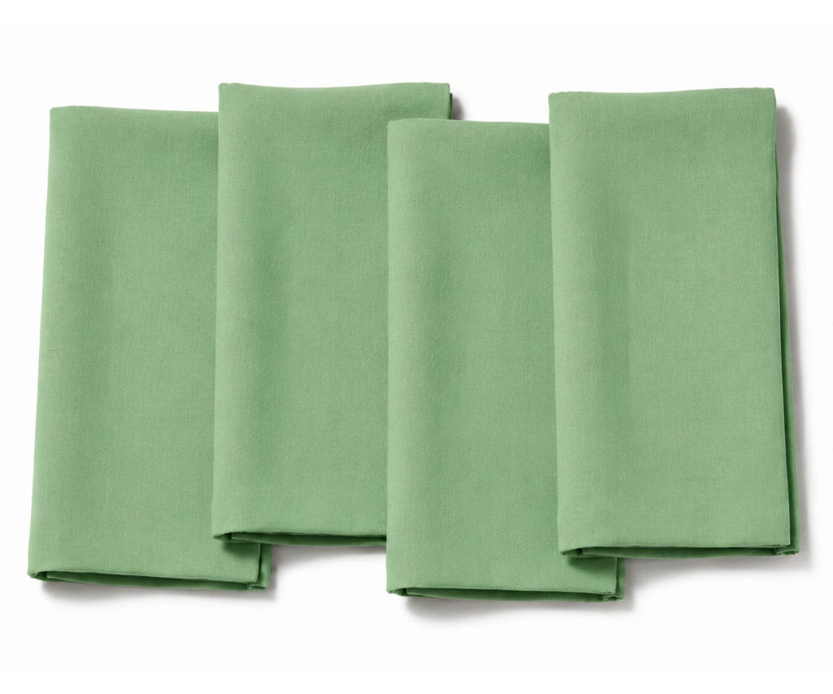 Set of four folded light sage green cotton dinner napkins arranged on a white background.