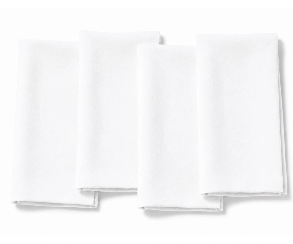 A set of four plain white fabric dinner napkins, neatly folded and displayed side-by-side against a clean white background.