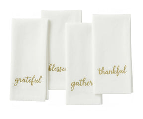 White sentiment embroidered table napkin with gold stitched holiday phrases for Christmas dining.