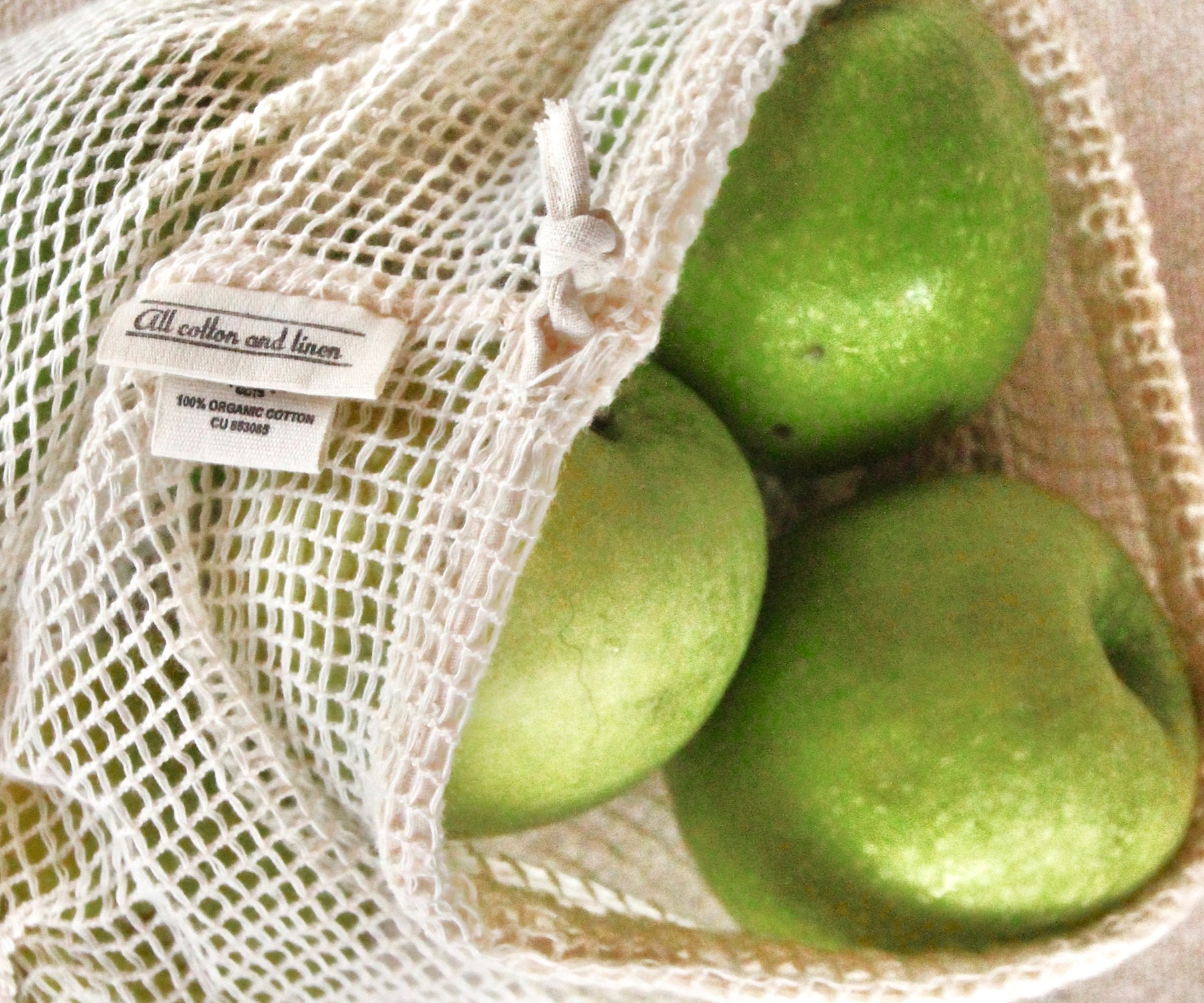 Green apples visible through a reusable mesh produce bag