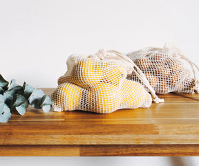 Two reusable mesh produce bags with fresh fruit on a wooden table