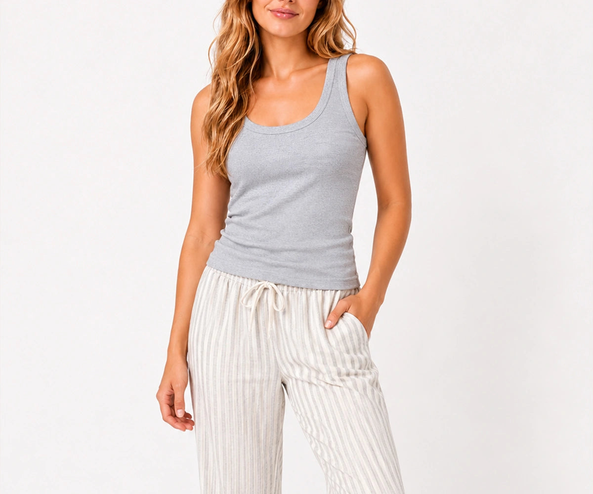 Woman wearing a heather grey ribbed cotton tank top paired with striped drawstring pajama pants