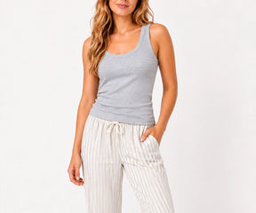 Woman wearing a heather grey ribbed cotton tank top paired with striped drawstring pajama pants