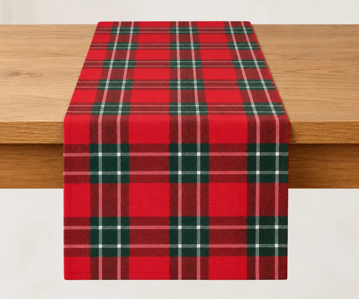 Red, green and black tartan cotton table runner draped over a wooden dining table, styled for Christmas dinner, winter entertaining, and festive holiday decor.