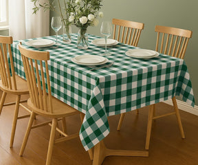 Dining table set with a green and white checkered tablecloth, plates, glasses, and a vase of flowers.