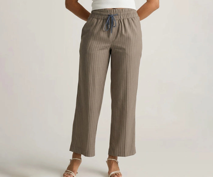 Front view of a model wearing high-waisted dark beige wide-leg cotton linen trousers with thin vertical stripes, a navy drawstring tie, and white strappy sandals.