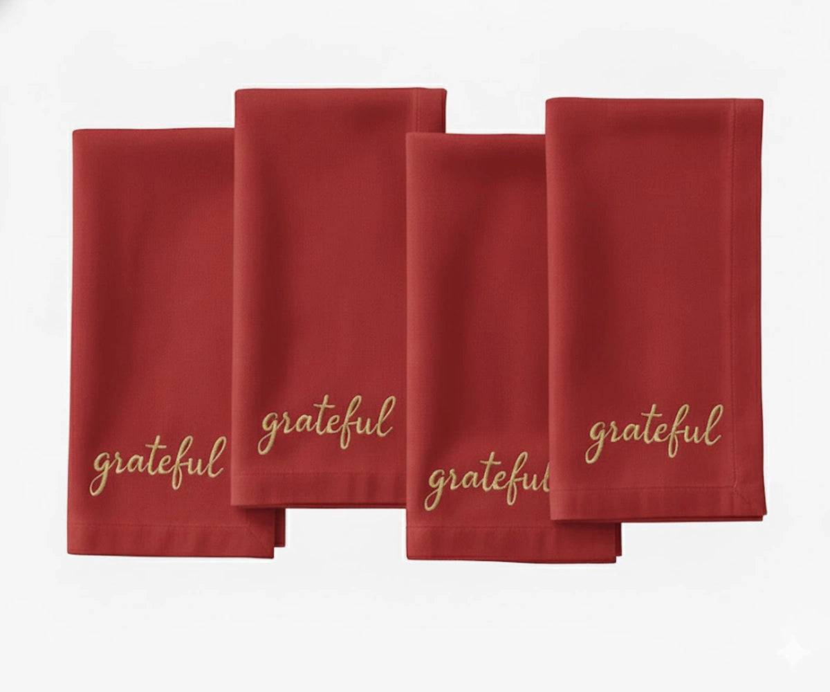 Dark red cloth napkin with beige “Grateful” embroidery for Christmas dining.