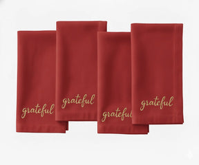 Dark red cloth napkin with beige “Grateful” embroidery for Christmas dining.