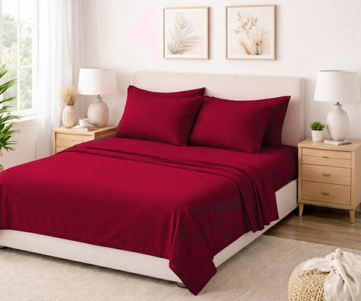 Premium deep burgundy plain bed sheet set on a neatly made bed with neutral decor, beige nightstands, and warm, bright lighting.