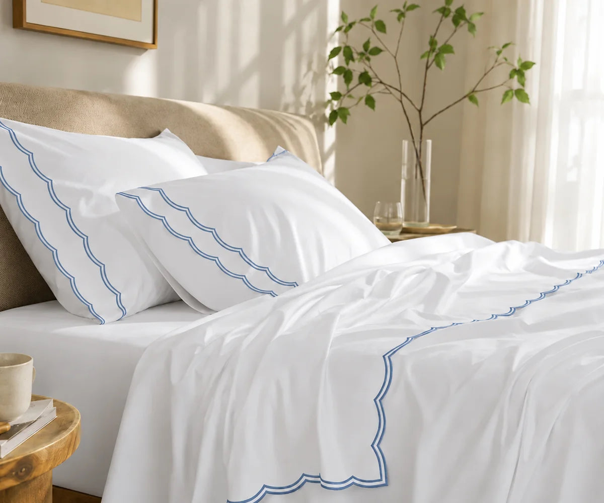 White cotton bedding set featuring dusty blue scalloped edge embroidery on pillows and flat sheet.