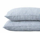 Pair of stacked pillows in dusty blue and white striped linen pillowcases against a plain white background.