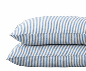 Pair of stacked pillows in dusty blue and white striped linen pillowcases against a plain white background.