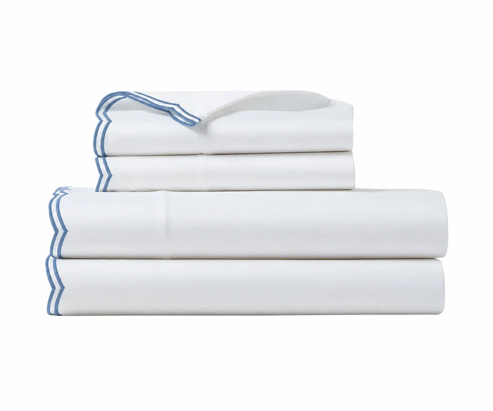 Stack of crisp white cotton bed sheets with blue scalloped embroidery details.   