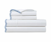 Stack of crisp white cotton bed sheets with blue scalloped embroidery details.   