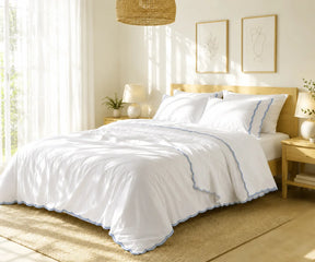 White cotton bedspread set with dusty blue scalloped edge embroidery styled on a bed in a bright bedroom.
