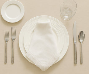 Dining table setting with white plates, silver cutlery, and a white napkin on a beige background