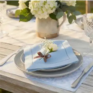 A styled outdoor table setting featuring a light blue folded napkin on a gray charger plate
