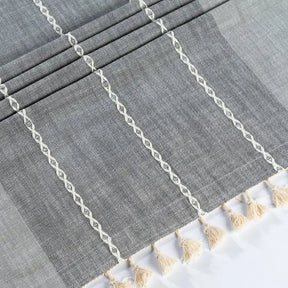 Gray striped tablecloth with white lace trim and beige tassels on a white background