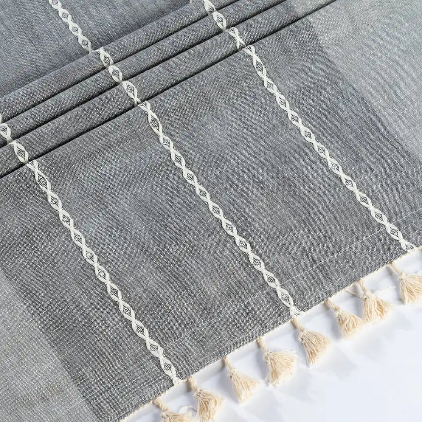 Gray striped tablecloth with white lace trim and beige tassels on a white background