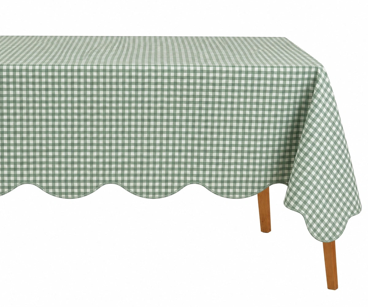 Sage green and white small checkered cotton tablecloth with a decorative scalloped edge draped over a table.