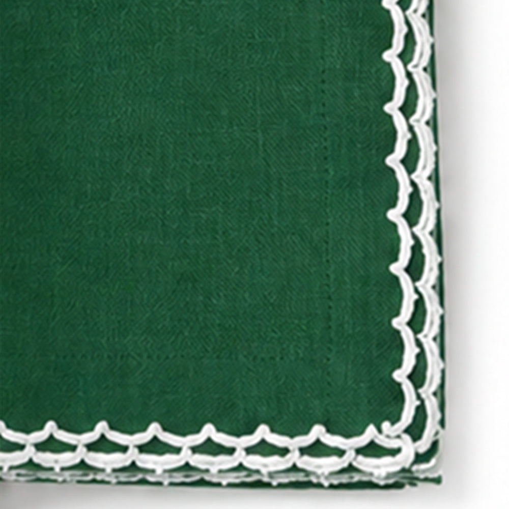 A close-up of a  green cotton napkin with a white scalloped embroidered border.