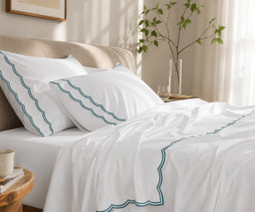 Close-up of white pillowcases and flat sheet with  green scalloped embroidery.