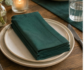 Dark green hemstitched table napkins styled on dining table, washable cotton cloth napkins for weddings, dinner parties, and farmhouse table decor