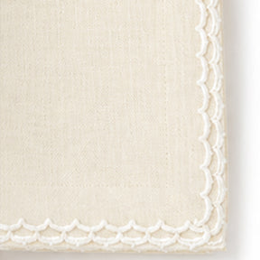 Close-up of a ivory colored woven fabric corner with a decorative white scalloped embroidered border.