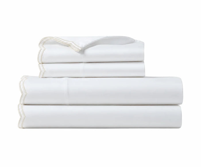 Folded white cotton sheet set with ivory scalloped embroidered trim.