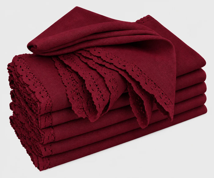 A neat stack of folded burgundy cotton cloth napkins featuring delicate lace trim and cutwork edges