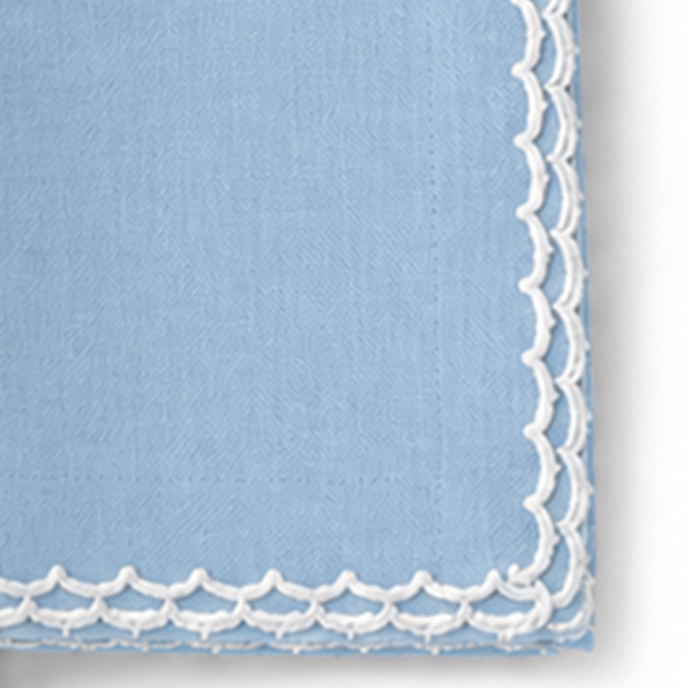 Close-up of a light blue cotton napkin featuring a white scalloped embroidered edge.