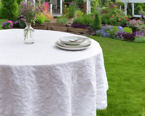 White linen round tablecloth styled outdoors with plates and a vase – ideal for garden or patio dining.