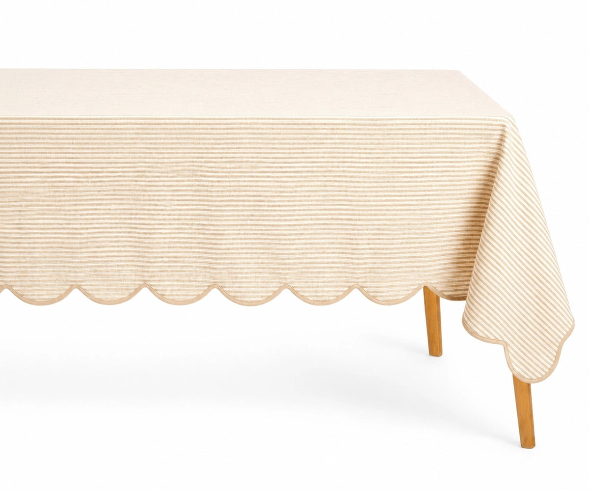 Natural beige and white thin striped linen tablecloth with a decorative scalloped edge draped over a table