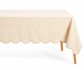 Natural beige and white thin striped linen tablecloth with a decorative scalloped edge draped over a table